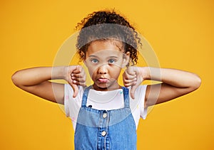 Studio portrait mixed race girl giving thumbs .down isolated against a yellow background. Cute hispanic child posing