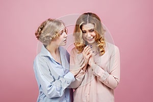 Studio portrait on pink background of two young girls. A friend comforting a crying girl and explains that all will be well.