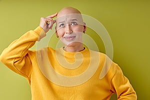 Studio portrait of pretty bald woman pondering over something touching head