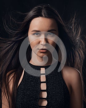 Studio portrait of pretty brunette woman with long hair flying on black background.