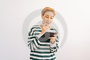 Studio portrait of pretty young woman writing down in notebook diary remind memories and make list of dreams standing on