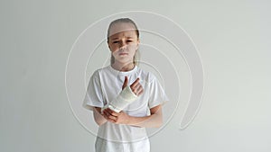 Studio portrait of sad cute little girl massaging forearm with expression of pain on face looking at camera standing on