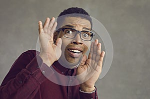 Studio portrait of a scared young black man in glasses looking at the camera and panicking