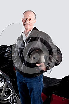 Studio portrait of a senior man standing by his motorcycle isolated on white.