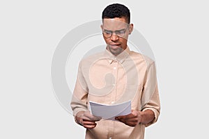 Studio portrait of serious African American young businessman in casual shirt analyzing financial reports posing on white studio