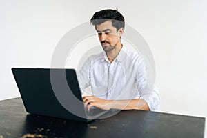 Studio portrait of serious focused businessman in shirt working on laptop computer, typing on keyboard sitting at desk