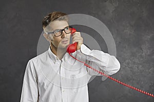 Studio portrait of serious focused man talking on landline phone and looking up thoughtfully.