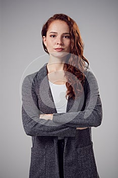 Studio Portrait Of Serious Young Businesswoman With Folded Arms Against Plain Background