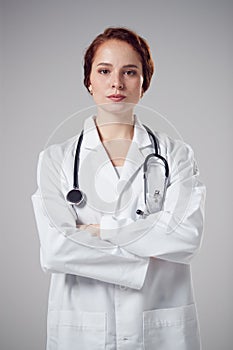 Studio Portrait Of Serious Young Female Doctor Wearing White Coat Against Plain Background