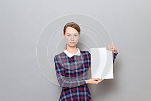 Studio portrait of serious young woman holding white blank paper sheet