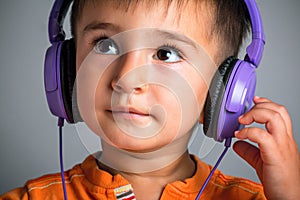 Studio portrait of a small funny boy with brown eyes in headphones listening to music on a gray background, emotions of joy, surpr