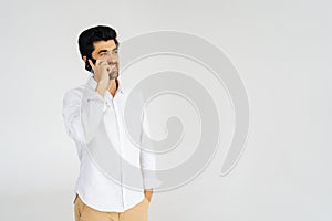 Studio portrait of smiling bearded young man talking smartphone, having conversation on mobile phone, holding and using