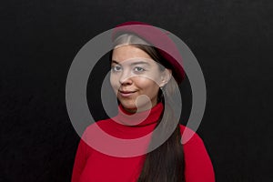 Studio portrait of a smiling beautiful young girl in a beret and a red sweater on a black background.