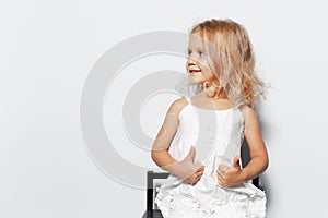 Studio portrait of smiling child girl with blonde hair on white background. Showing thumbs up, looking away. Copy space concept.