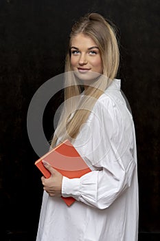 Studio portrait of a smiling girl 20-25 years old with a book in her hands on a dark background.