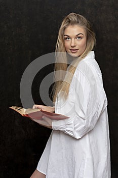 Studio portrait of a smiling girl 20-25 years old with a book in her hands on a dark background.