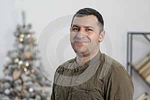 Studio portrait of a smiling man of 30-35 years of oriental appearance on the background of a Christmas tree.