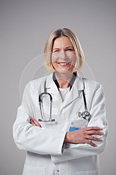 Studio Portrait Of Smiling Mature Doctor Wearing White Coat Against Plain Background