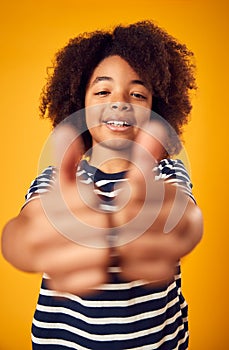 Studio Portrait Of Smiling Young Boy Making Thumbs Up Gesture Shot Against Yellow Background