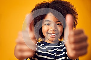 Studio Portrait Of Smiling Young Boy Making Thumbs Up Gesture Shot Against Yellow Background