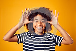 Studio Portrait Of Smiling Young Boy Pulling Funny Face Shot Against Yellow Background