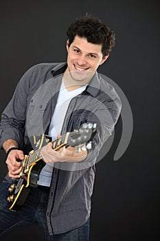 studio portrait of a smiling young man playing guitar