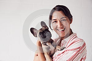 Studio Portrait Of Smiling Young Woman Holding Affectionate Pet French Bulldog Puppy