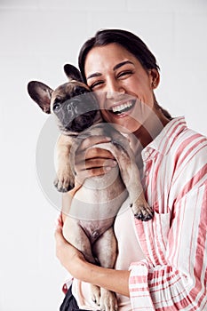 Studio Portrait Of Smiling Young Woman Holding Affectionate Pet French Bulldog Puppy