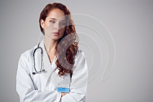 Studio Portrait Of Stressed Young Female Doctor Wearing White Coat Against Plain Background