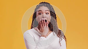 . Studio portrait of surprised african american woman covering her open mouthed in amazement, orange background