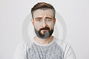 Studio portrait of uncertain and disappointed bearded male adult, looking at camera with sad look and frowned eyebrows