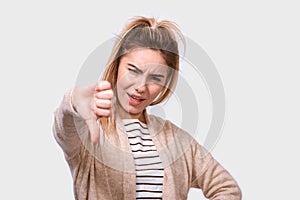 Studio portrait of unhappy woman giving thumbs down gesture looking with negative expression and disapproval.