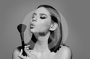 Studio portrait of a woman applying cosmetic tonal foundation on face using makeup brush. Beautiful girl doing photo