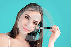 Studio portrait of a woman applying cosmetic tonal foundation on face using makeup brush. Beautiful girl doing photo
