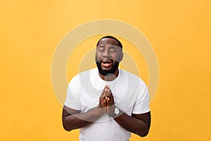 Studio portrait of young African American man in white shirt, holding hands in prayer, looking at the camera with