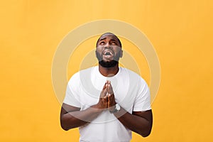 Studio portrait of young African American man in white shirt, holding hands in prayer, looking at the camera with