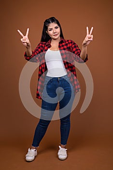 Studio portrait of young beautiful Asian woman making peace sign