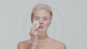 Studio portrait of young, beautiful and natural blond woman applying skin care cream. Face lifting, cosmetics and make