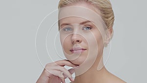 Studio portrait of young, beautiful and natural blond woman applying skin care cream. Face lifting, cosmetics and make