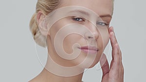 Studio portrait of young, beautiful and natural blond woman applying skin care cream. Face lifting, cosmetics and make