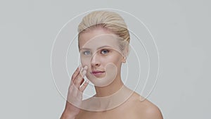 Studio portrait of young, beautiful and natural blond woman applying skin care cream. Face lifting, cosmetics and make