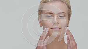 Studio portrait of young, beautiful and natural blond woman applying skin care cream. Face lifting, cosmetics and make