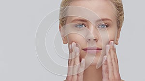 Studio portrait of young, beautiful and natural blond woman applying skin care cream. Face lifting, cosmetics and make