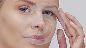 Studio portrait of young, beautiful and natural blond woman applying skin care cream. Face lifting, cosmetics and make