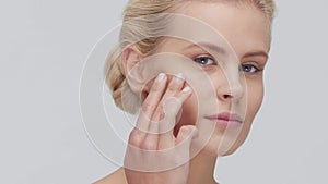 Studio portrait of young, beautiful and natural blond woman applying skin care cream. Face lifting, cosmetics and make