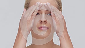 Studio portrait of young, beautiful and natural blond woman applying skin care cream. Face lifting, cosmetics and make