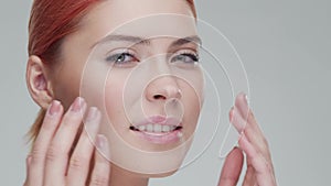 Studio portrait of young, beautiful and natural redhead woman applying skin care cream. Face lifting, cosmetics and make