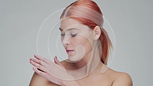 Studio portrait of young, beautiful and natural redhead woman applying skin care cream. Face lifting, cosmetics and make