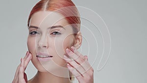 Studio portrait of young, beautiful and natural redhead woman applying skin care cream. Face lifting, cosmetics and make