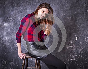 Studio portrait of young beautiful woman in a leather skirt sitting on high stool.